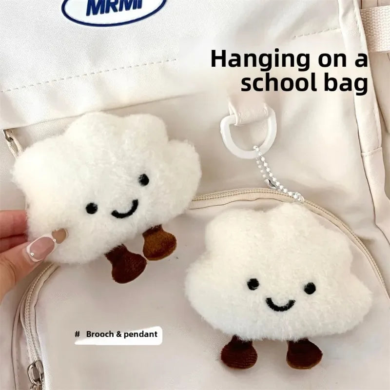 A white cloud-shaped plush keychain with embroidered features is hanging on a school bag.