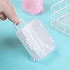A hand is holding a clear plastic miniature doll suitcase with a handle on a light blue background.