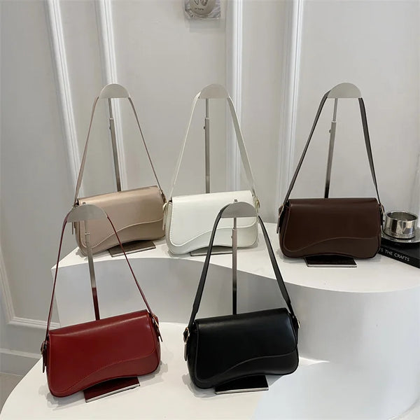 Four vintage curved flap shoulder bags in various colors including beige white brown and red displayed on a white pedestal.