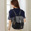 Une femme portant un haut bleu marine et un pantalon beige, vue de dos, portant un sac à dos en cuir microfibre noir.