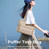 Une femme portant un haut clair et une longue jupe tient un sac fourre-tout rembourré beige à l'extérieur.