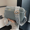 A light blue-green vegan PU crossbody bag with a patterned strap is held by a person.