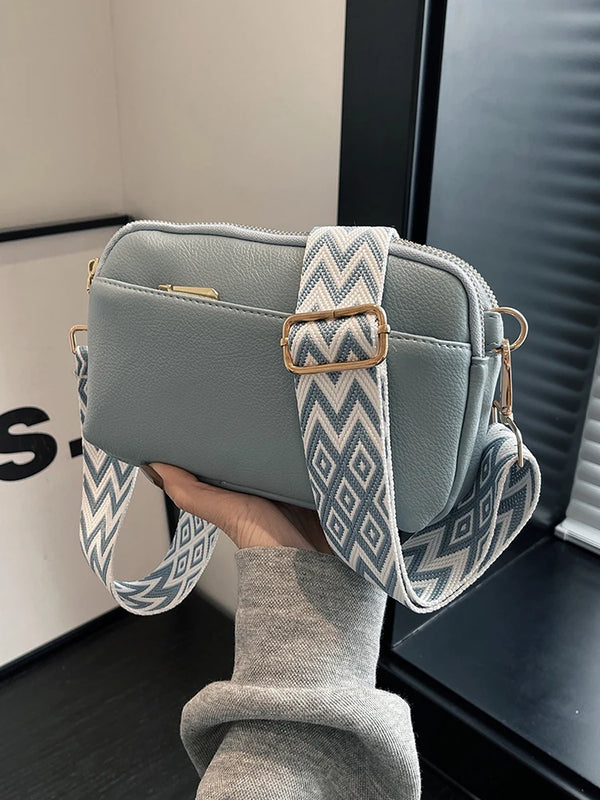 A light blue-green vegan PU crossbody bag with a patterned strap is held by a person.