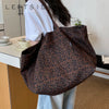 A brown leopard print canvas tote bag is shown hanging on a person's shoulder in a bright indoor setting.