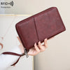 A brown leather RFID blocking travel wallet is being held by a hand against a light background.