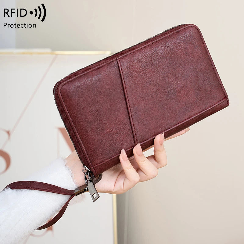A brown leather RFID blocking travel wallet is being held by a hand against a light background.