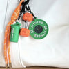 Orange nylon fitness keychain with a green bottle holder and an orange weight, attached to a white leather surface.