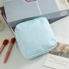 Light blue striped storage pouch next to makeup brushes and a book.
