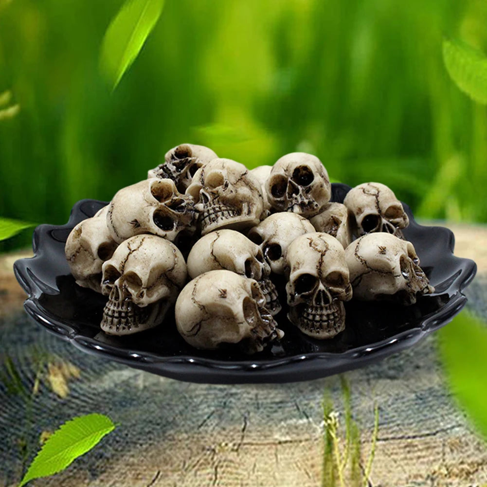 Pila de esculturas de cráneo de resina realista para decoración de Halloween sobre un plato oscuro con fondo verde y frondoso