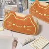 An orange caramel cat plush pencil pouch resting on a white surface next to other stationery items.