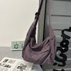 A purple cotton canvas shoulder crossbody bag hanging against a light wall and a vertical striped surface.