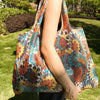 A person holds a colorful patterned fabric shopping tote bag outdoors on a grassy lawn.