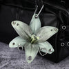 A realistic pale green orchid flower keychain attached to a black leather bag.