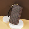 A brown patterned PU leather zippered wallet resting on a white cylindrical stand.