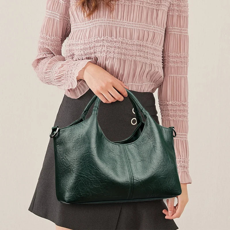 A woman holds a dark green leather casual crossbody shoulder bag with a zip closure.