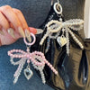 A close-up of a Y2K bowknot pearl keychain with pink and clear beads attached to a black leather bag.