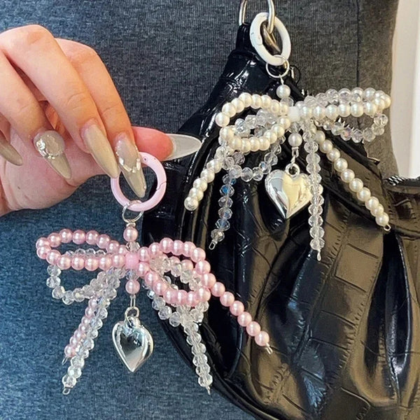 A close-up of a Y2K bowknot pearl keychain with pink and clear beads attached to a black leather bag.
