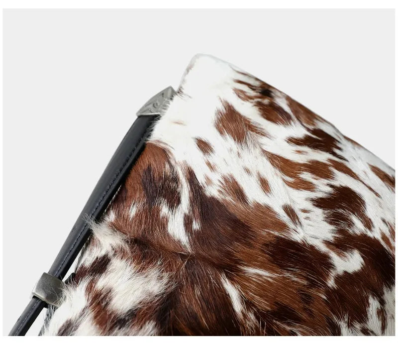 A close-up of a brown and white spotted cowhide leather crossbody bag.