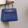 A navy blue crocodile pattern tote bag with gold hardware being held by a person in a light colored jacket.