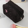 A black quilted cosmetic bag with a zipper and a pink bow detail is shown next to a makeup brush.