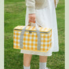 A person holds a yellow and white checkered insulated picnic tote bag outdoors.