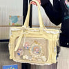 A light yellow transparent shoulder tote bag with lace trim and decorative elements is being held by a person.