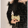 A close-up of a woman wearing a black sequined dress with a gold bow knot accessory and a chain strap.