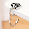 A round silver metal bag hanger with a black and white floral pattern is displayed on a white surface.