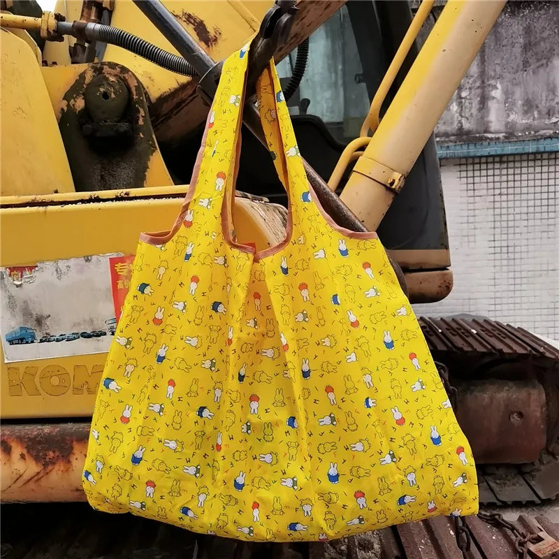 A bright yellow Miffy folding shopping bag is displayed in a workshop setting.
