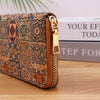 A brown patterned leather wallet with a gold zipper is shown resting on a wooden surface next to some stacked books.