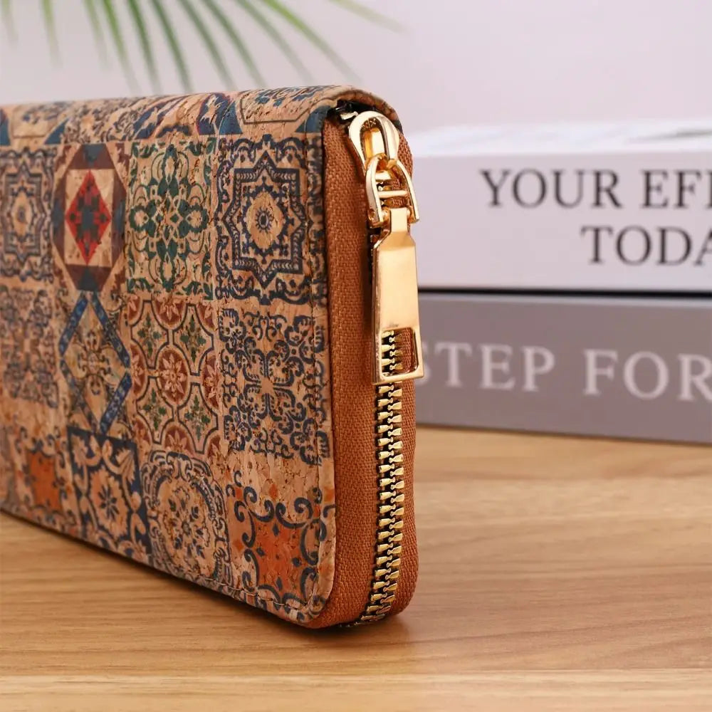A brown patterned leather wallet with a gold zipper is shown resting on a wooden surface next to some stacked books.
