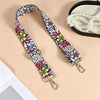 A floral patterned nylon crossbody bag strap with metal buckles is displayed next to a pearl necklace.