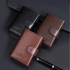 A brown leather card holder and a black leather wallet are displayed on a dark surface.