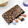 A leopard print zippered cosmetic bag lying open with makeup brushes and a cosmetic product nearby.