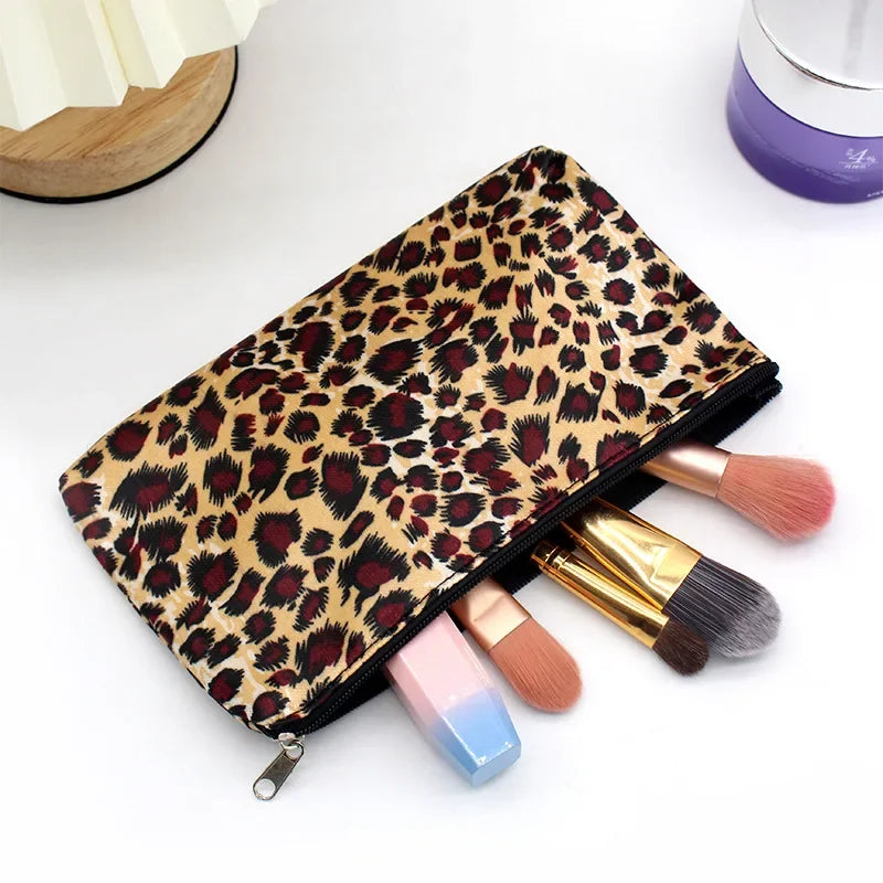 A leopard print zippered cosmetic bag lying open with makeup brushes and a cosmetic product nearby.