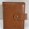 A brown crocodile leather ring binder notebook with a stitched closure.