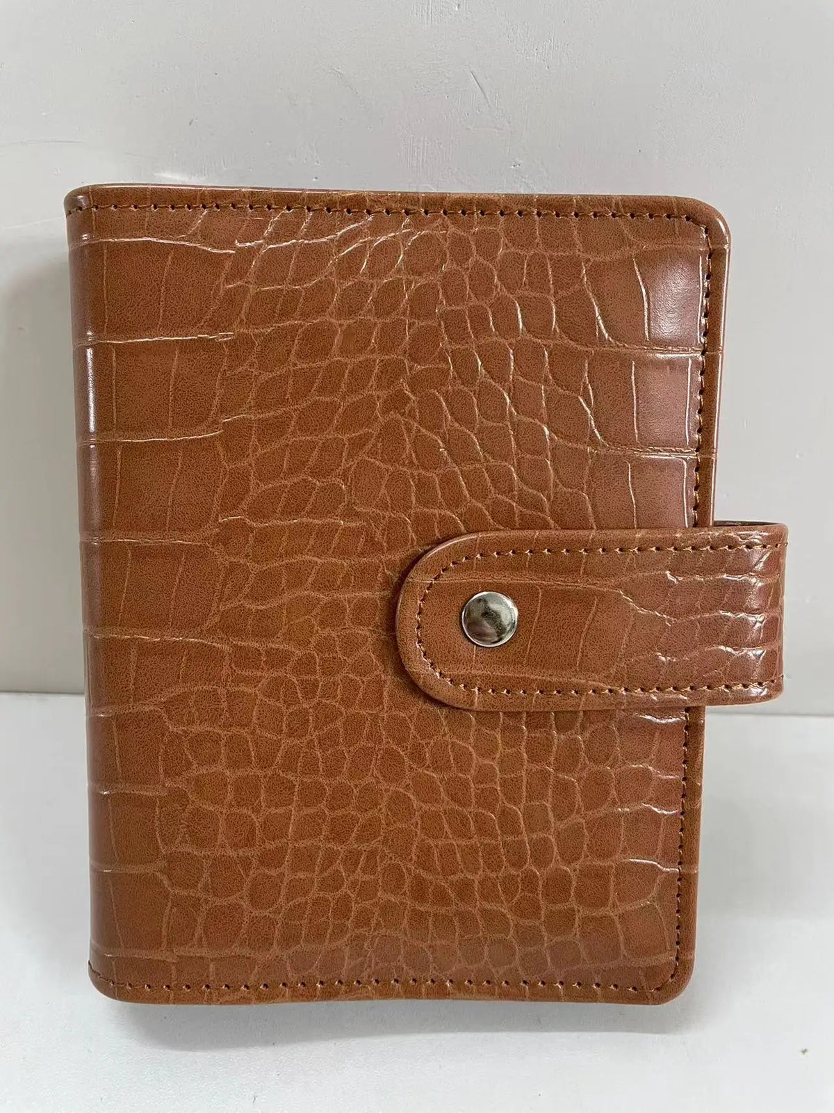 A brown crocodile leather ring binder notebook with a stitched closure.