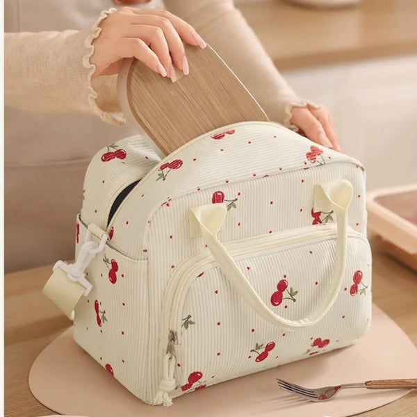 A light cream insulated lunch bag with a white vertical stripe pattern and red floral accents is being held by a person.