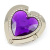 A heart-shaped silver metal fold-over bag hook with a purple gemstone inset.