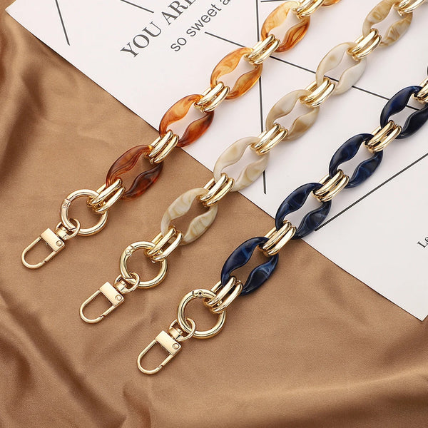 Exhibición de cadenas de correas de bolsas de acrílico ajustables en tonos dorados, marrones y azules sobre tela beige junto 