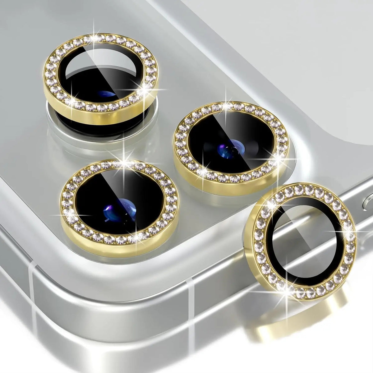 Four glitter diamond camera lens protectors with metal frames displayed on a silver surface.