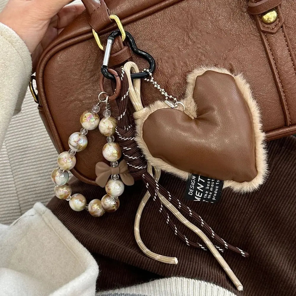 Brown leather heart pendant keychain with a long tassel attached to a brown leather bag.