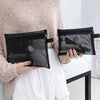 A person holds a black mesh cosmetic storage pouch in their hand, worn over a light sweater and white skirt.