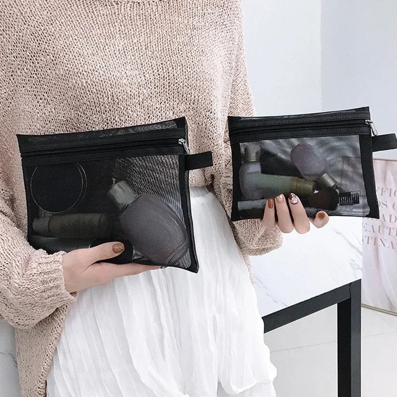 A person holds a black mesh cosmetic storage pouch in their hand, worn over a light sweater and white skirt.