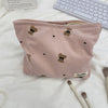 A pink corduroy clutch bag decorated with small teddy bear appliqués, resting on a white surface.