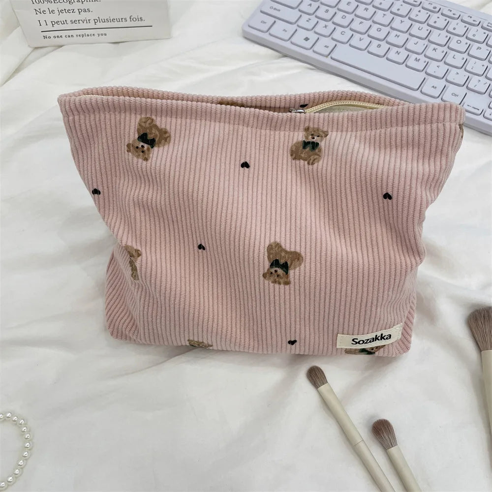 A pink corduroy clutch bag decorated with small teddy bear appliqués, resting on a white surface.