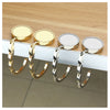 Four gold and silver folding alloy handbag hangers displayed on a wooden surface.