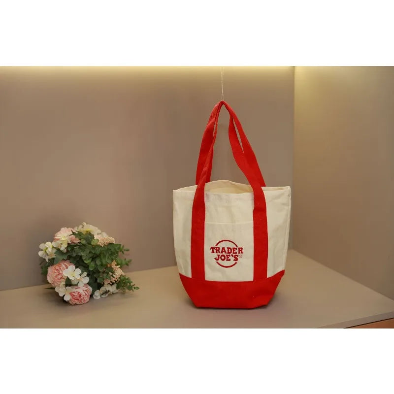A white canvas bag with red handles and a red logo is displayed on a light surface.