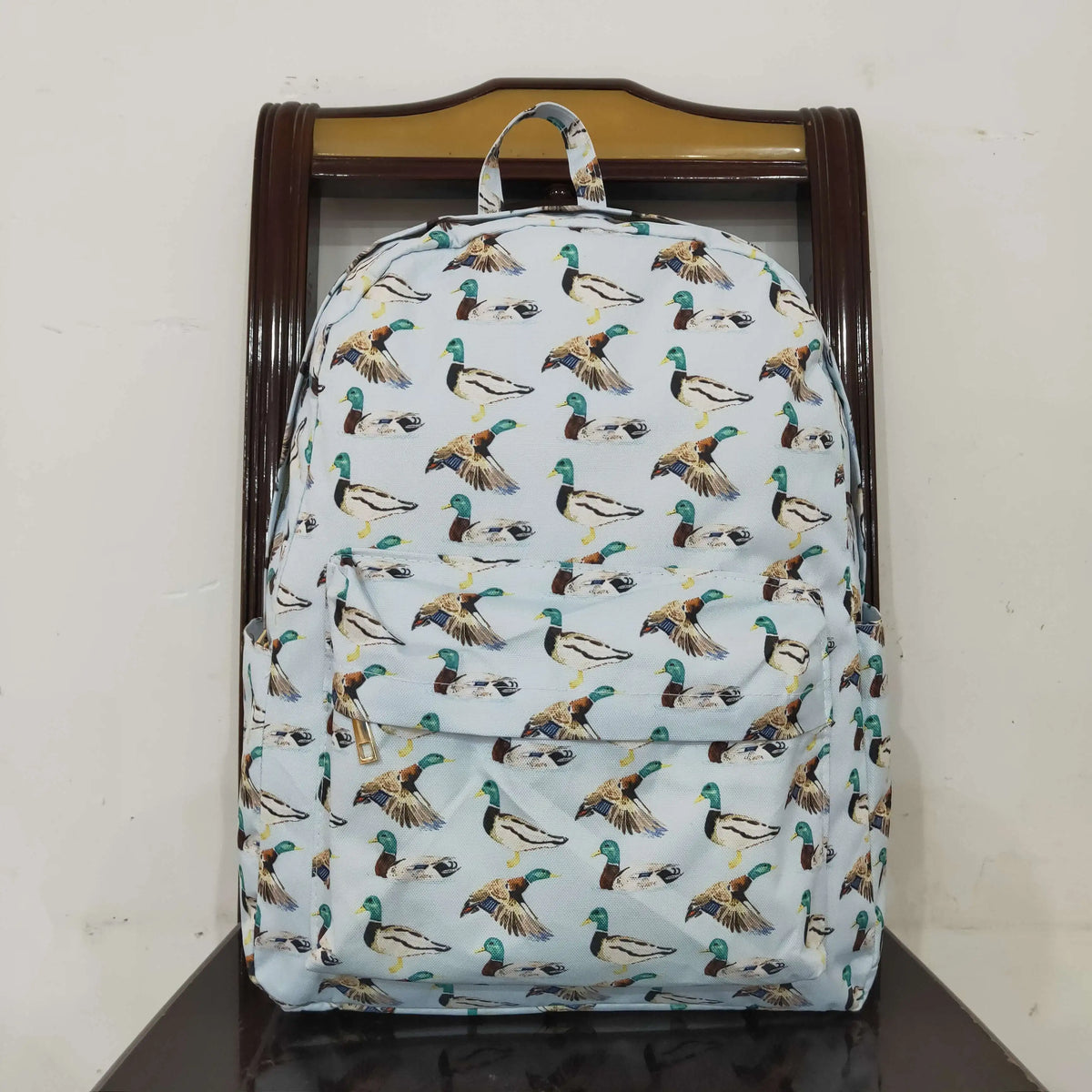 A light blue and green patterned toddler backpack with animal prints displayed on a wooden hanger.