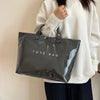 A person holds a black transparent waterproof PVC tote bag against a white background.